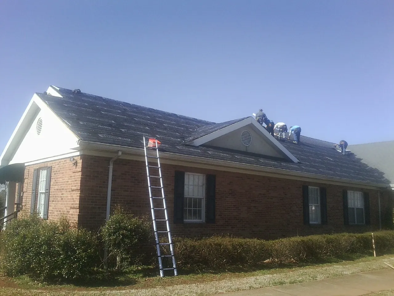 Crew tearing shingles off a brick ranch roof with a ladder set — Emergency Roof Repair work by our crew in Pond Creek