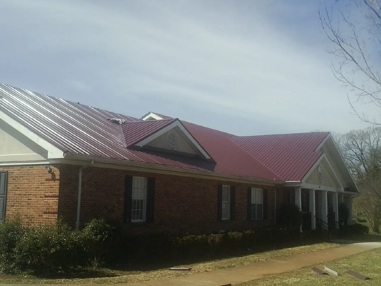 Red metal roof with gabled entries on a long brick building, from a Hail Damage Roof Repair job in Pond Creek