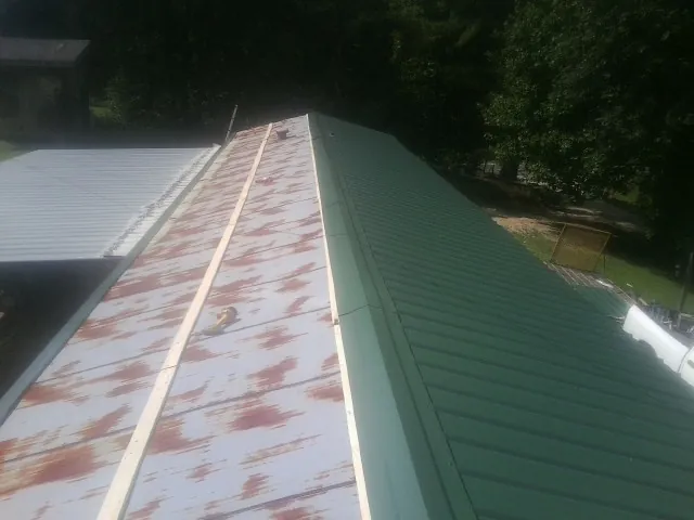 Old rusted panels beside newly installed green metal roofing — Wind Damage Roof Repair by Roofing Brothers in Pond Creek