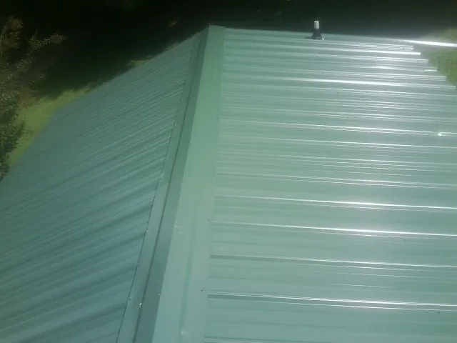 New green metal panels meeting at the ridge of a roof — Flat Roof Repair work by our crew in Pond Creek