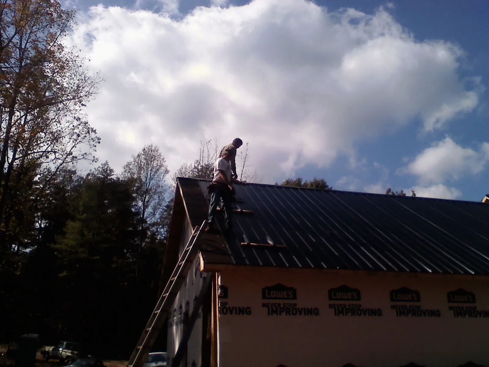 Roofer fastening dark metal panels high against a cloudy sky, from a Roof Inspection job in Pond Creek
