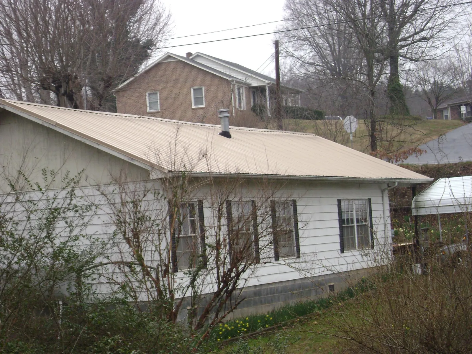 Tan metal roof on a white sided house set into a hillside — Commercial Roofing by Roofing Brothers in Pond Creek